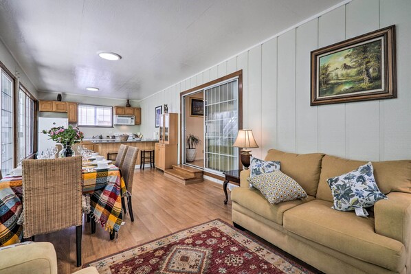 A spacious living room with a beige sofa, patterned throw pillows, and a dining area with a table set for six.