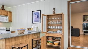 A kitchen with wooden cabinets, a microwave, a bar area with stools, and a glassware shelf. - Peaceful Oakland Oasis w/ Private Yard! (Oakland)