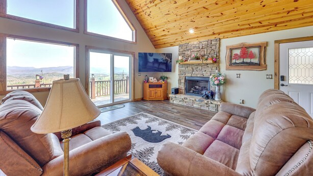 Ein geräumiges Wohnzimmer mit Ledersofas, einem Kamin, Steinverkleidungen und großen Fenstern mit Blick.