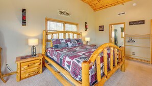 Ein hölzernes Bett mit Karo-Decke, ein Nachttisch mit Lampe, eine Holzkommode und ein Spiegel.