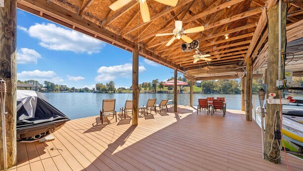 Une terrasse couverte avec un plancher en bois, des ventilateurs de plafond et une vue sur un lac.