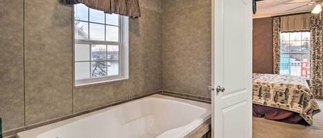 Un baño con una bañera grande, una ventana con vistas y una puerta que conduce a un dormitorio.