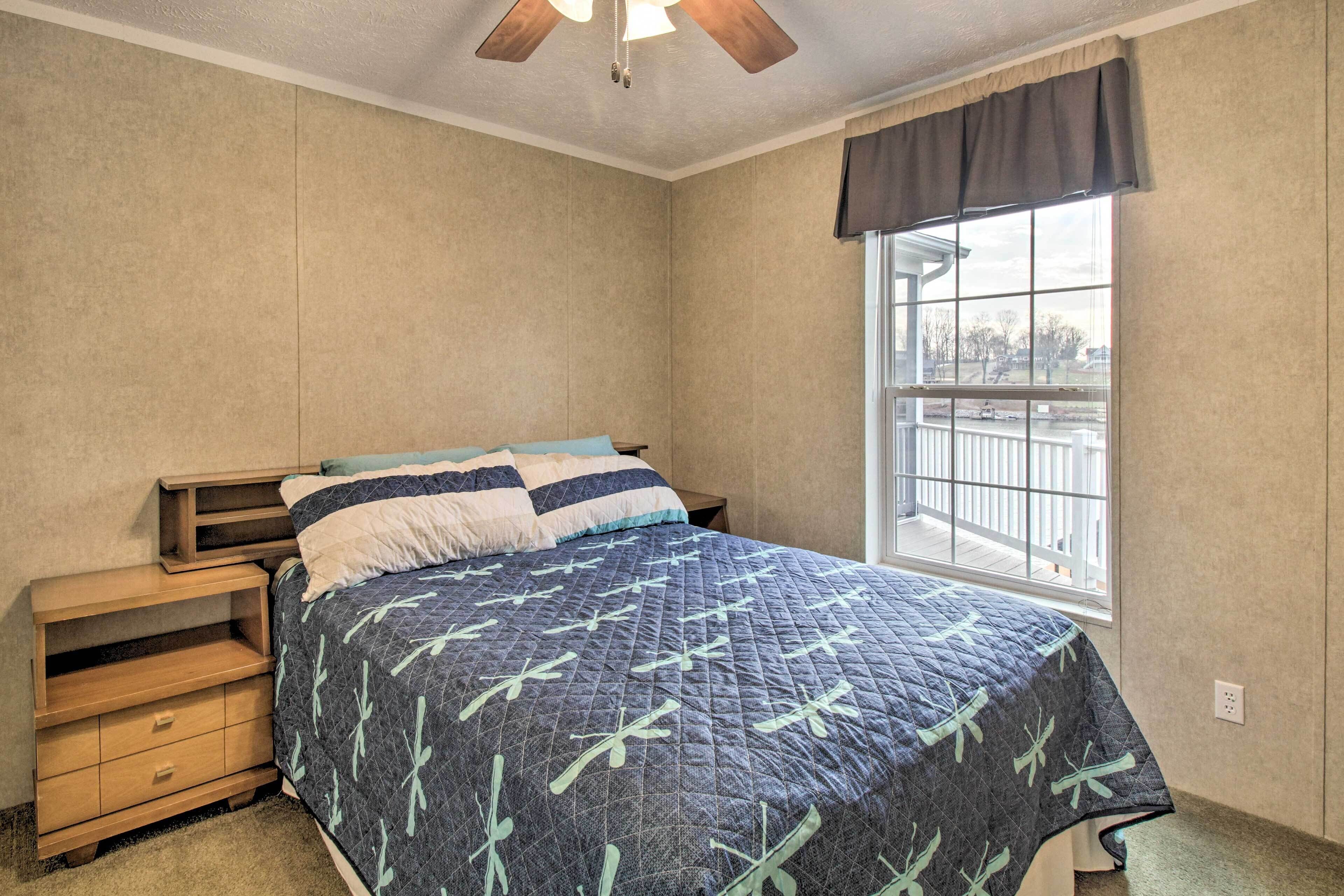 Quarto com cama, mesa de cabeceira, janela com vista e ventoinha no teto.