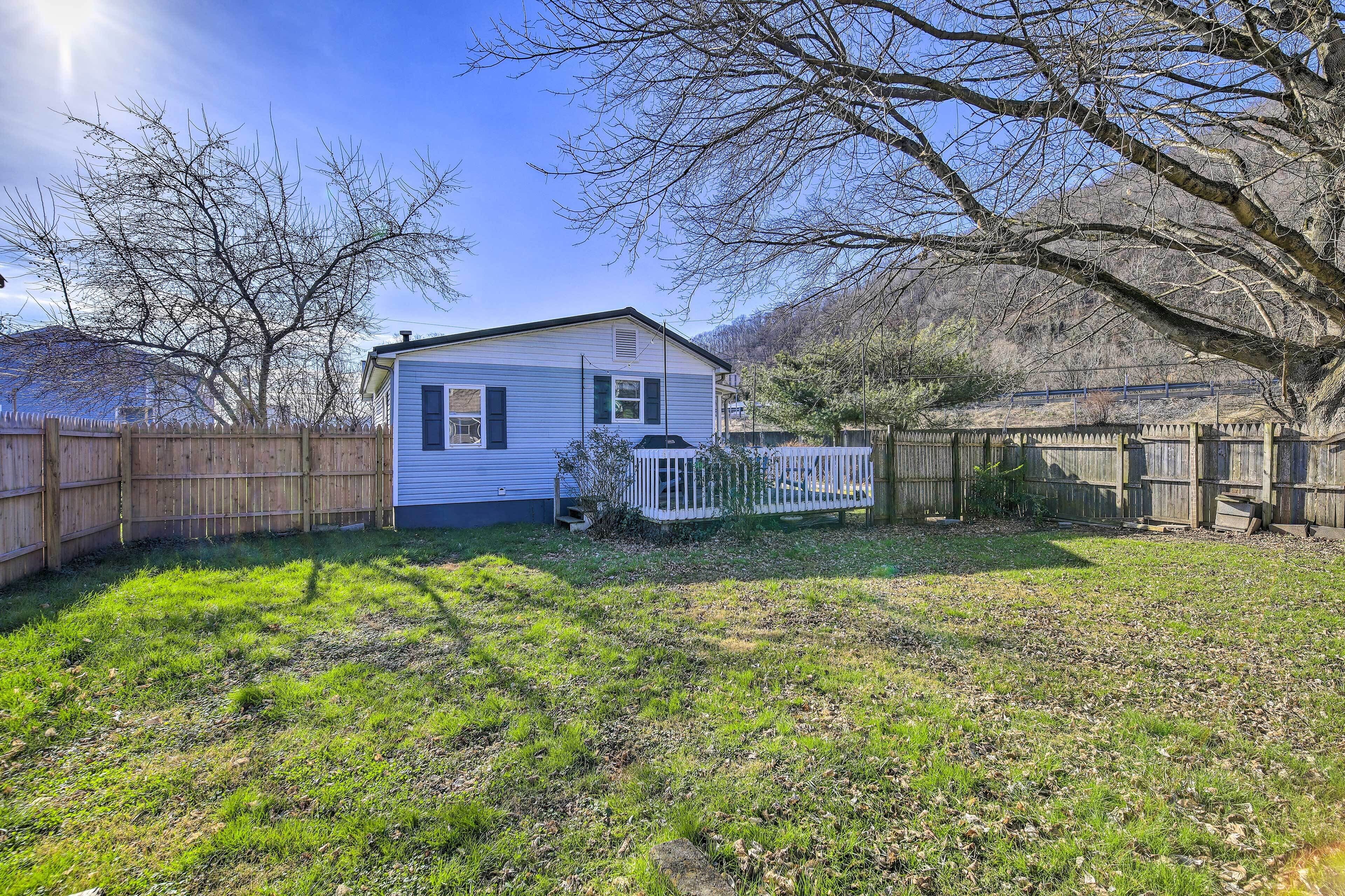 A single-story house with a fenced backyard, a wooden deck, and a large tree.