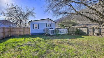 A single-story house with a fenced backyard, a wooden deck, and a large tree.