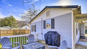 En uteplats med Adirondack-stolar och en grill, ett takförsett uteområde och ett hus med vit träpanel på utsidan.
