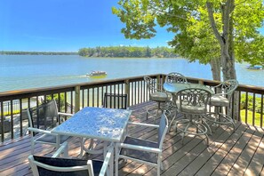 A wooden deck with a table and chairs, overlooking a lake with a boat in the distance. - Lakefront Grant Getaway w/ Deck + Fire Pit! (Grant)
