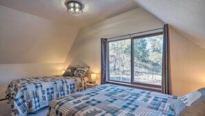 A bedroom with two beds, a window with a view of trees, and a ceiling light fixture. - Divide Cabin in the Heart of Colorful Colorado! (Divide)