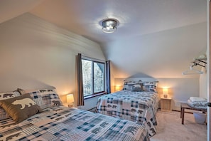Une chambre avec deux lits, une fenêtre, un luminaire au plafond, une table de chevet et une chaise.