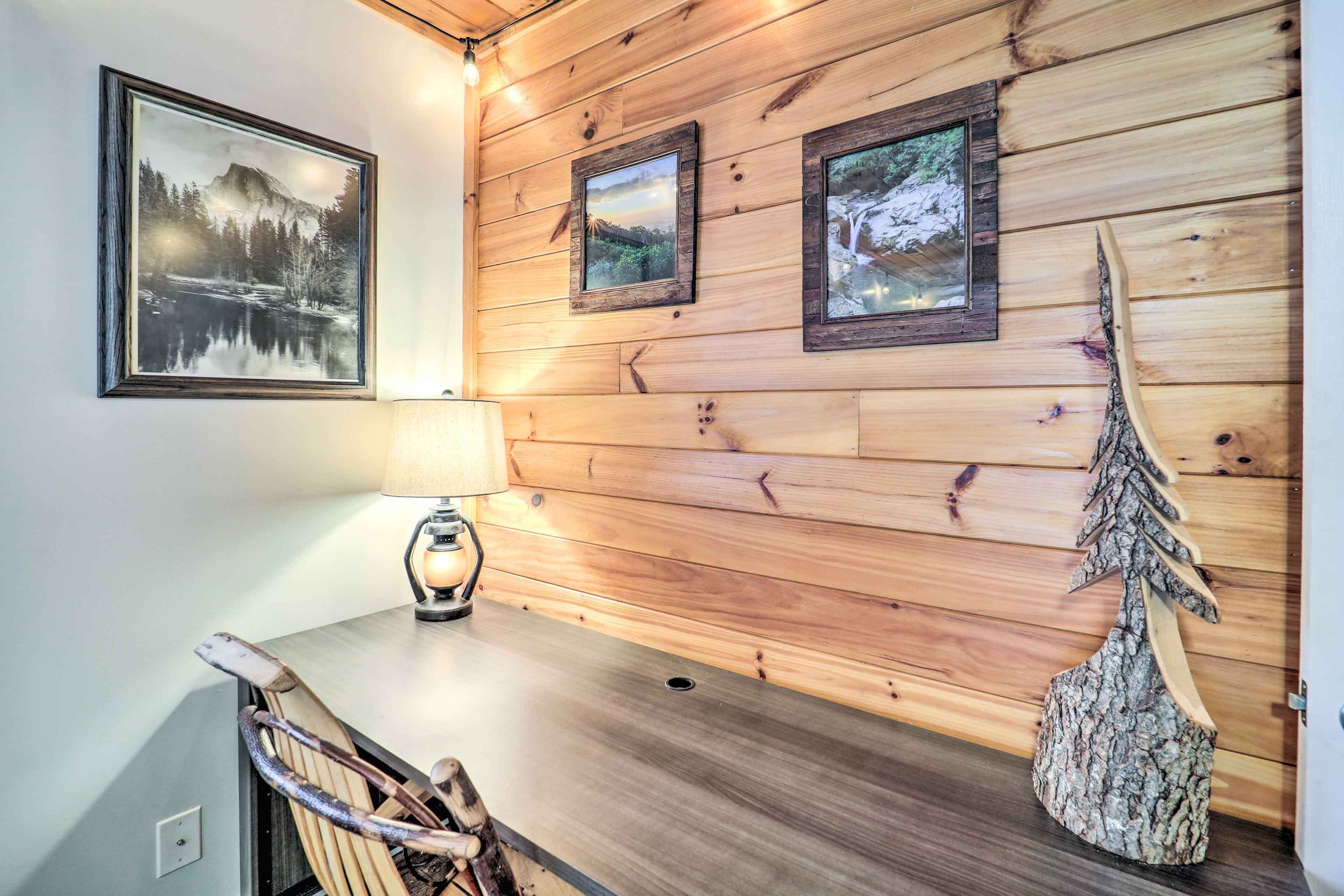 A wooden wall with framed pictures, a table with a lamp, and a carved wooden tree.
