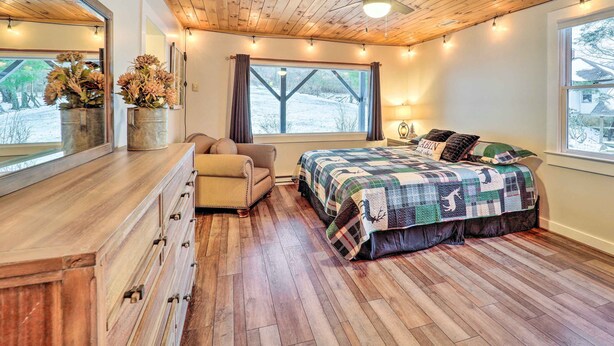 A bedroom with a wooden ceiling, a bed with a quilt, a dresser, a chair, and a window with curtains. - Mountain Retreat < 4 Mi to Downtown Boone! (Boone)