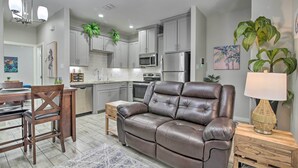 A modern kitchen with grey cabinets, a microwave, and a refrigerator. There is a dining area with a wooden table and chairs, and a brown leather sofa. - Private Patio: Edinburg Couple's Retreat! (Edinburg)
