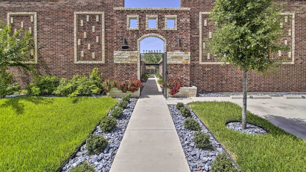 A brick building with a central archway, surrounded by a well-maintained garden with a pathway leading to the entrance. - Private Patio: Edinburg Couple's Retreat! (Edinburg)