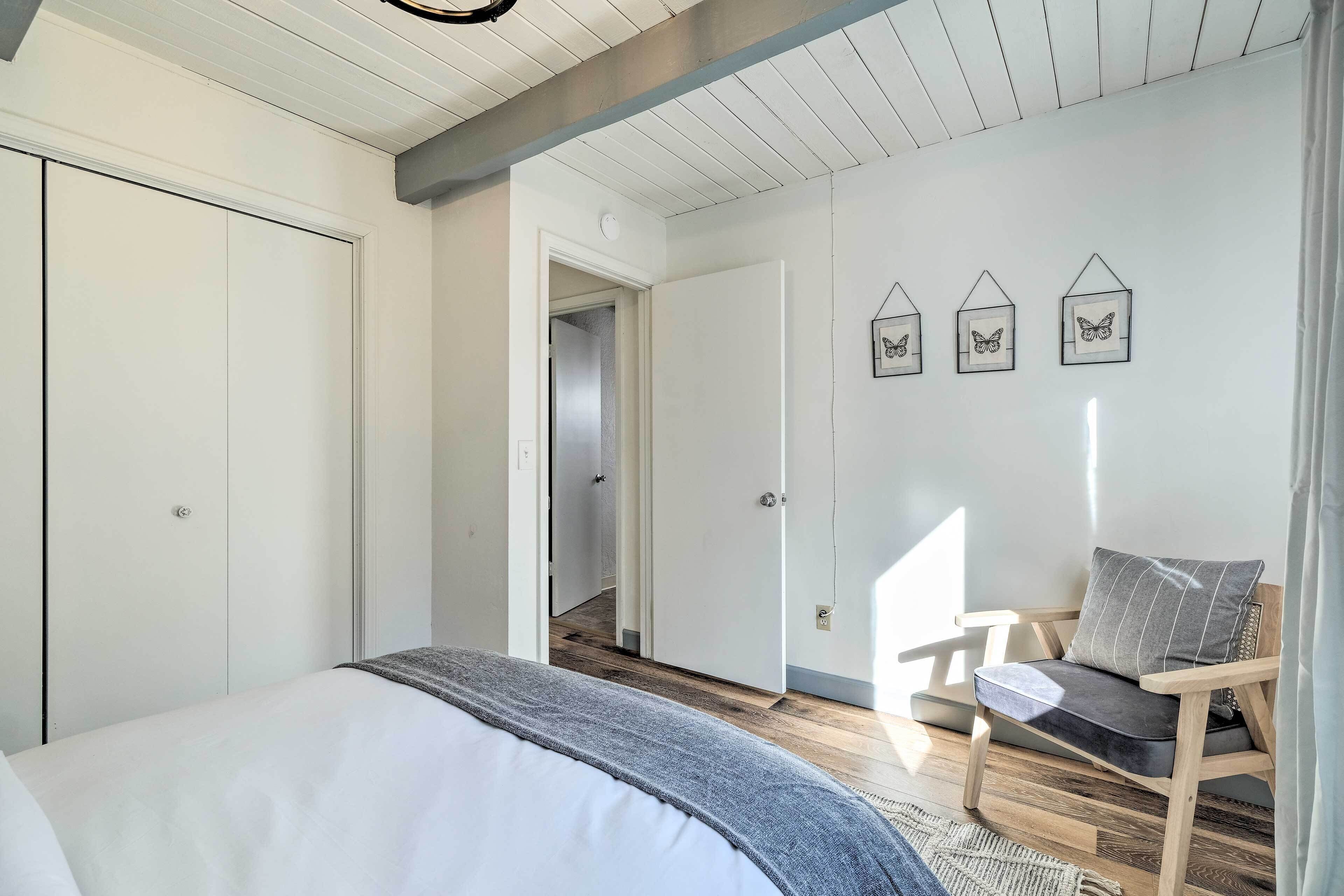 A bedroom with a bed, a wooden bench with cushions, a wall-mounted butterfly decoration, and a door leading to another room.