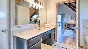 Een moderne badkamer met een grote spiegel, een lamp boven de wastafel en uitzicht op de aangrenzende ruimte.
