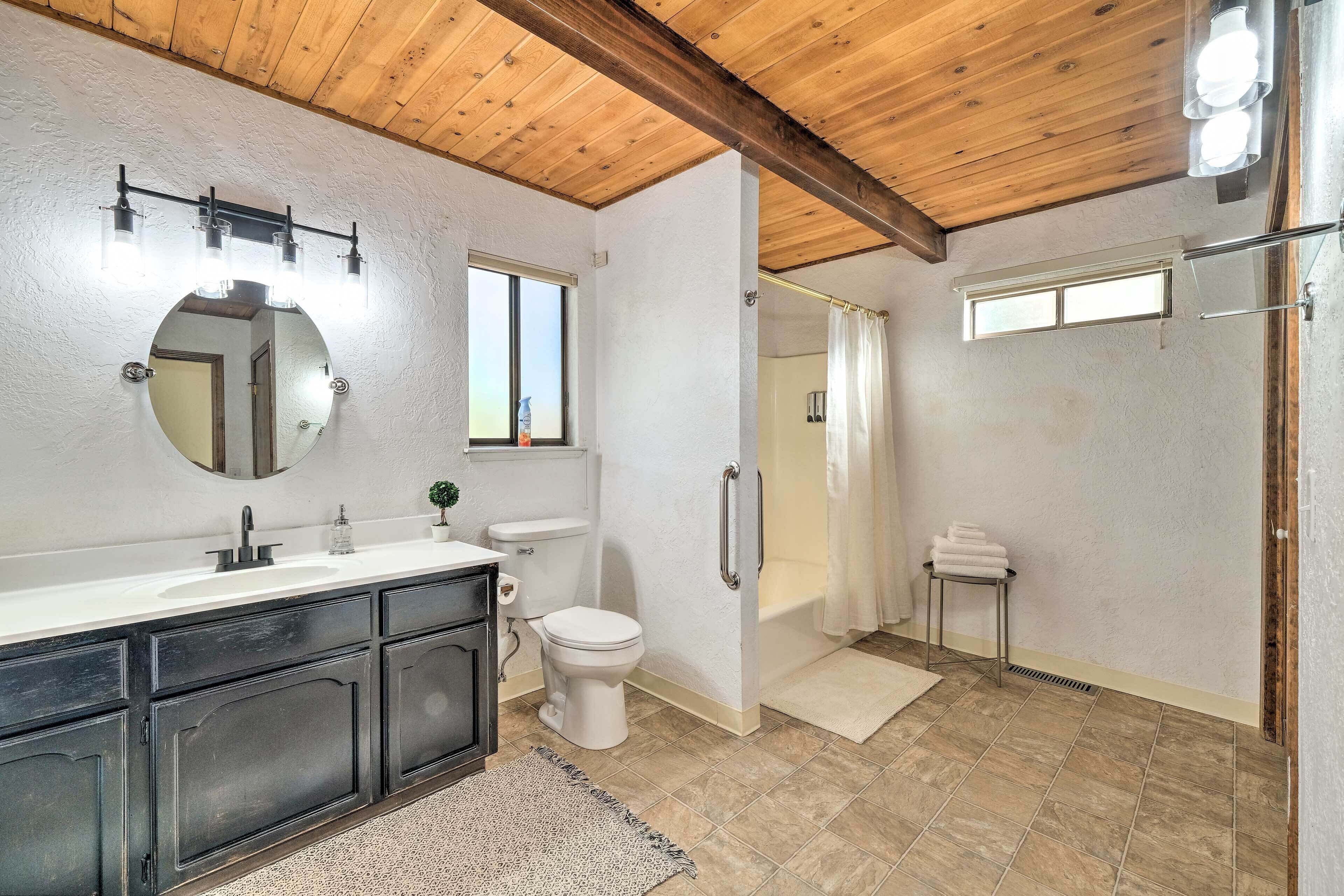 A bathroom with a wooden ceiling, a large mirror, a sink, a toilet, and a shower area.