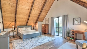Een slaapkamer met een schuine kap, een bed, een bureau en een groot raam.