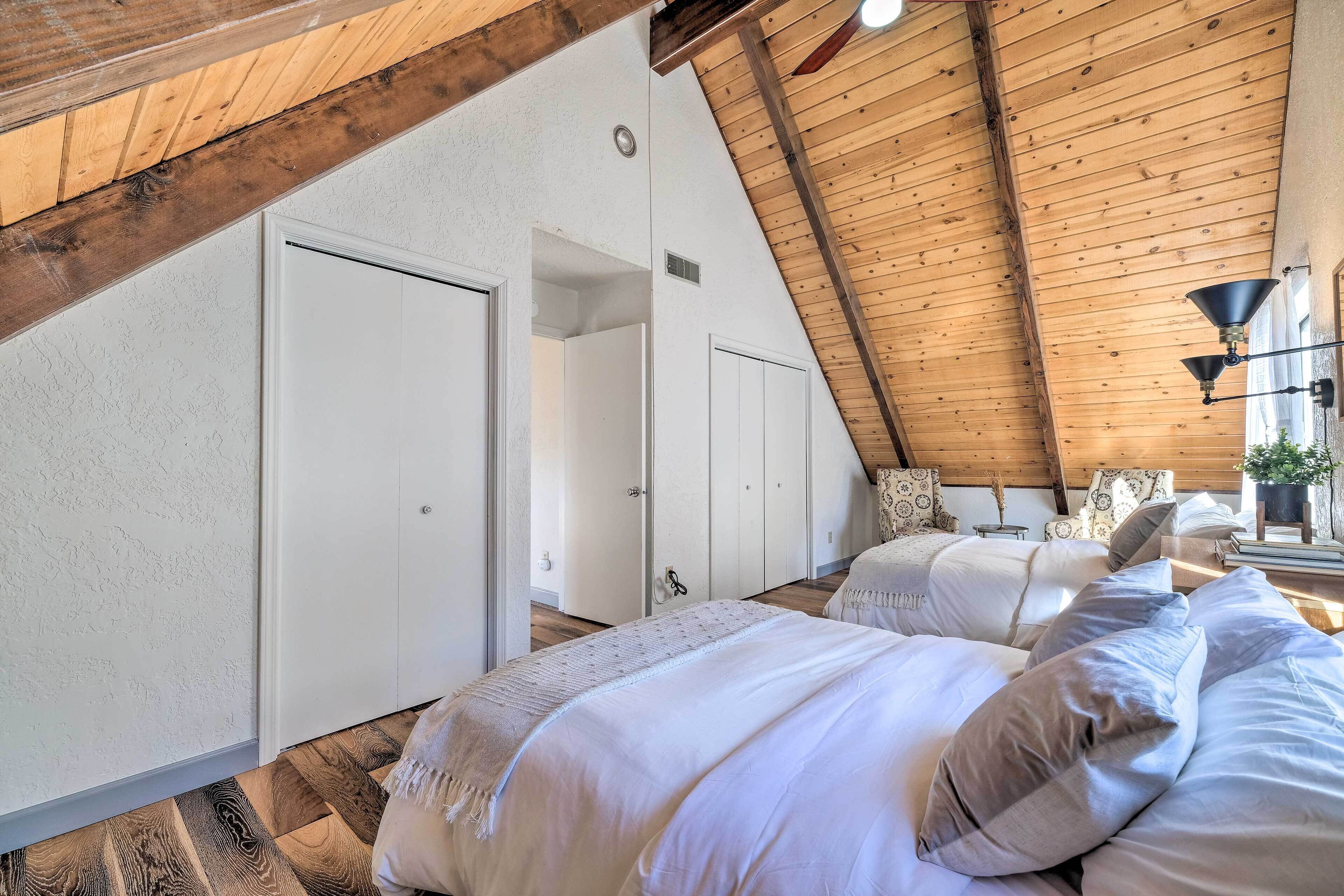 A bedroom with a sloped ceiling, wooden beams, white walls, and a large bed with multiple pillows.