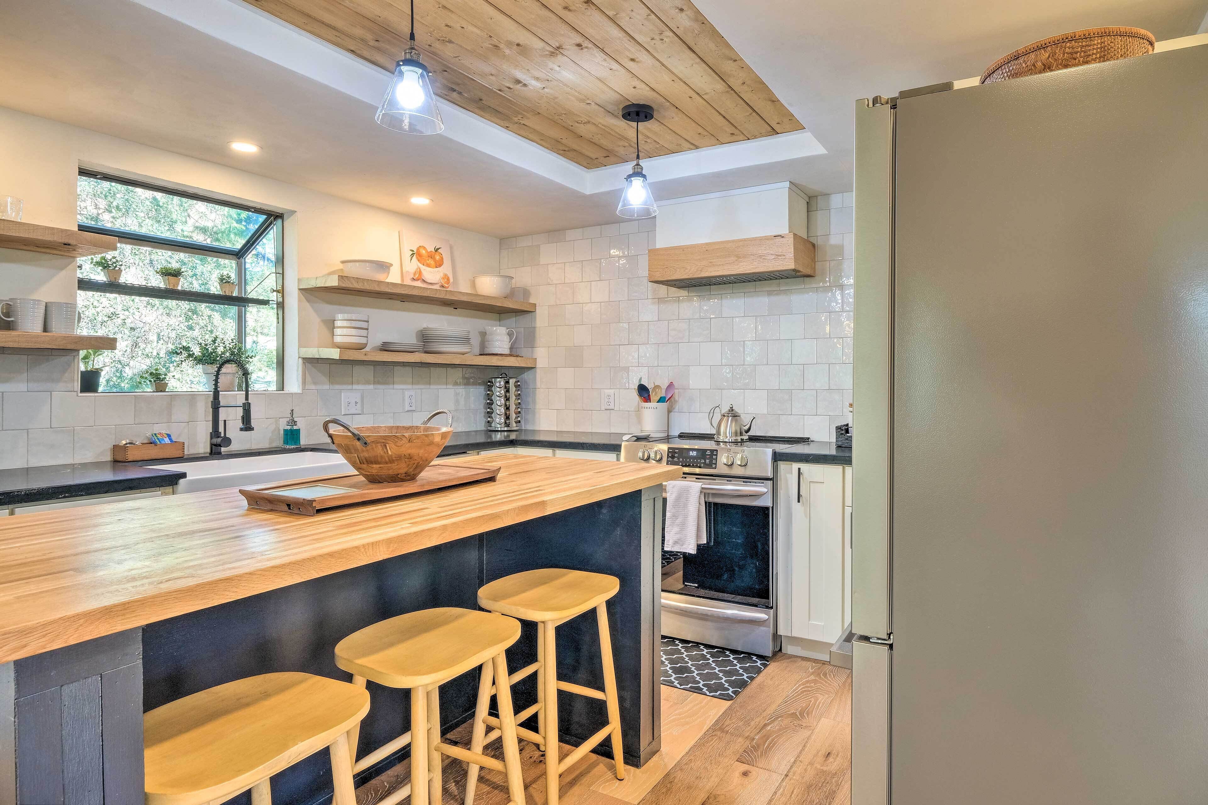 Una cocina moderna con una isla de madera, taburetes de bar, un ventanal grande y un horno empotrado.