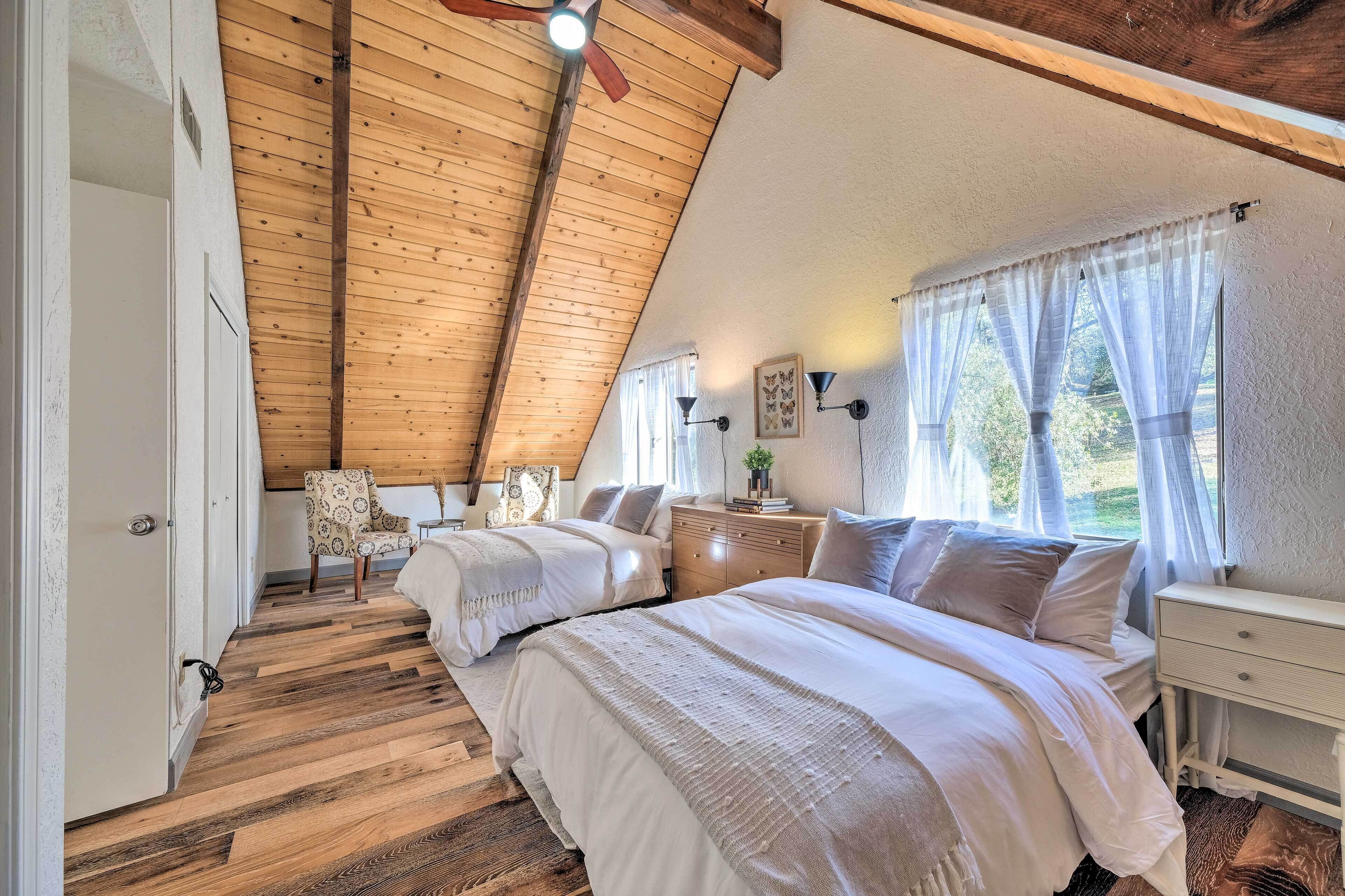 A bedroom with two beds, wooden flooring, a sloped ceiling, and a window with sheer curtains.