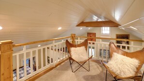 Ein Schlafzimmer im Loft-Stil mit hohen Decken, Holzbalken, einer weißen Geländer und zwei Ledersesseln mit weichen Kissen.
