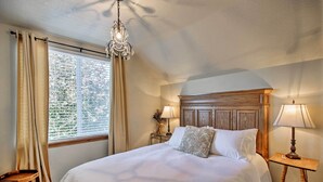 Un dormitorio ordenado con una cama grande, dos mesitas de noche con lámparas, un cabecero de madera y una ventana con cortinas.