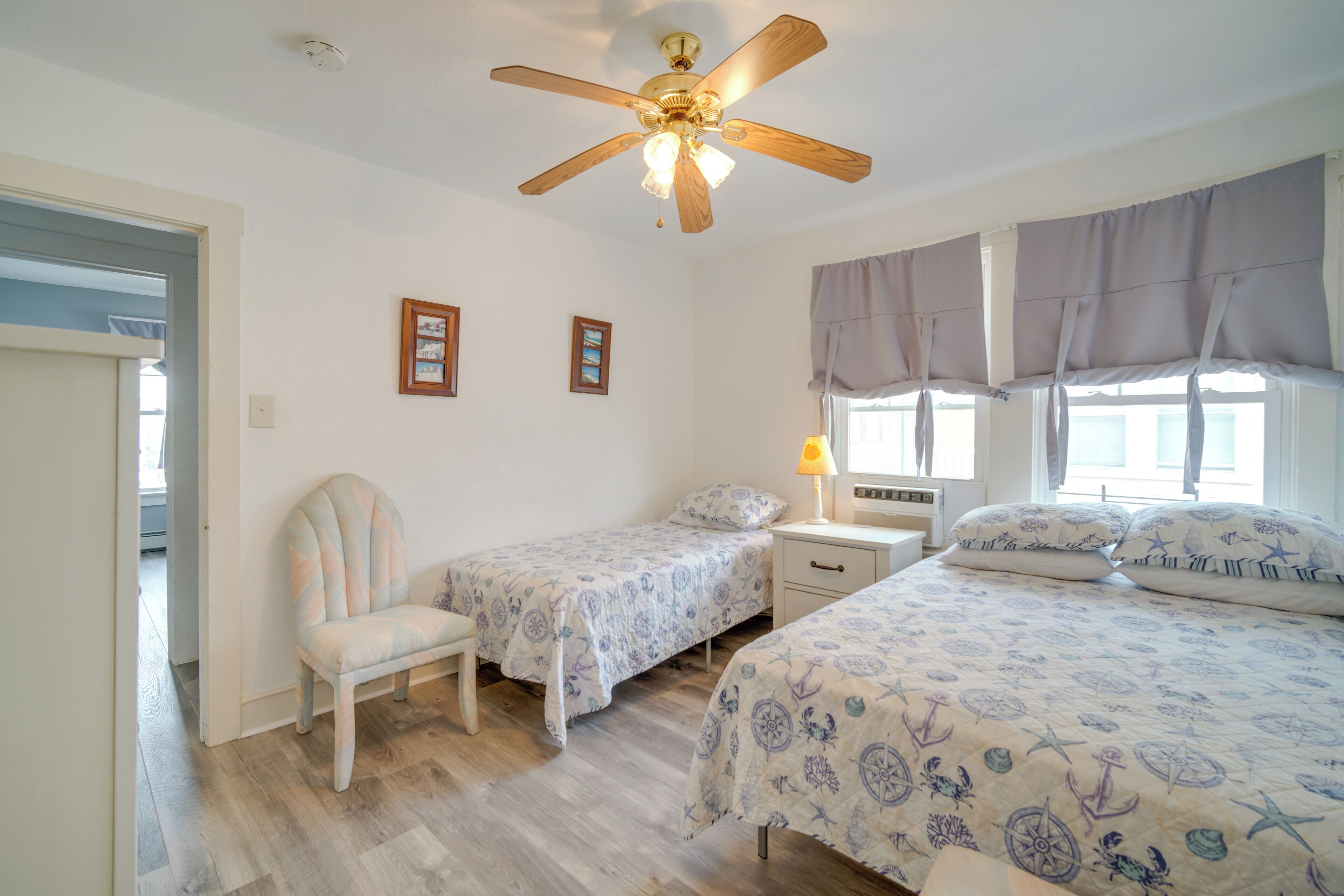 A bedroom with two single beds, a ceiling fan, a chair, a nightstand, and a window with curtains.