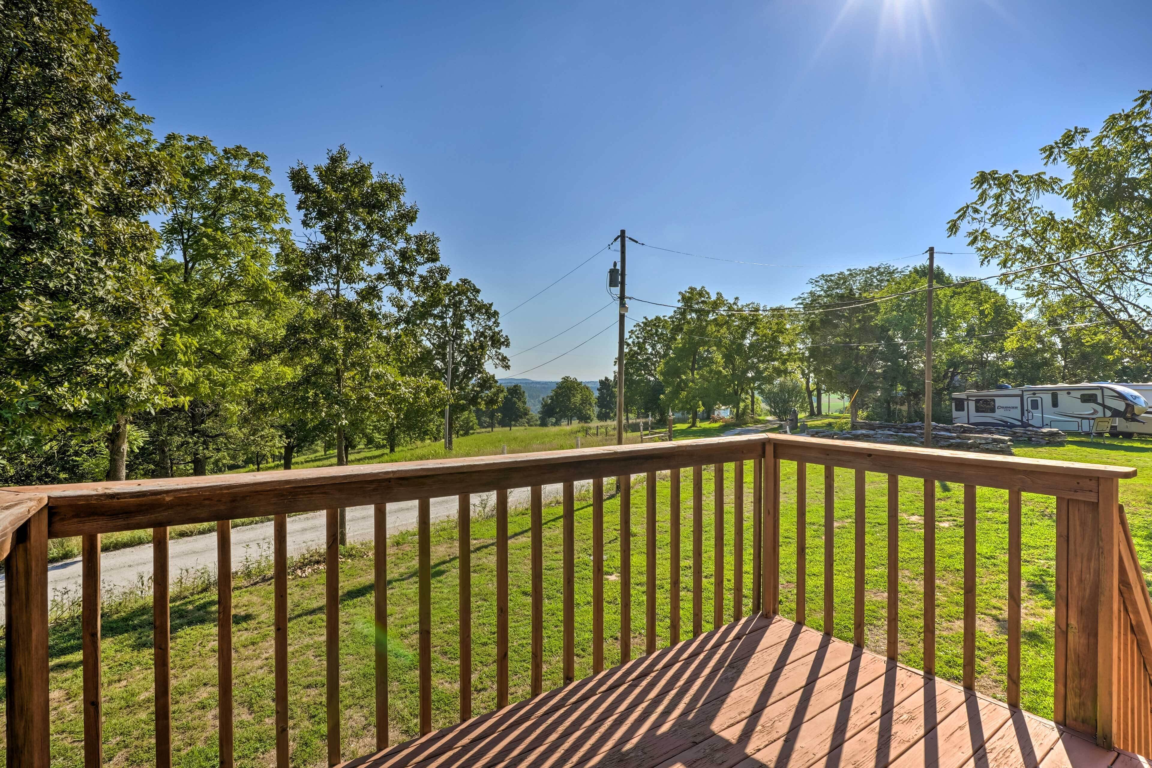 A wooden deck with a view of a grassy area and a recreational vehicle in the distance.