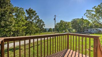 A wooden deck with a view of a grassy area and a recreational vehicle in the distance.