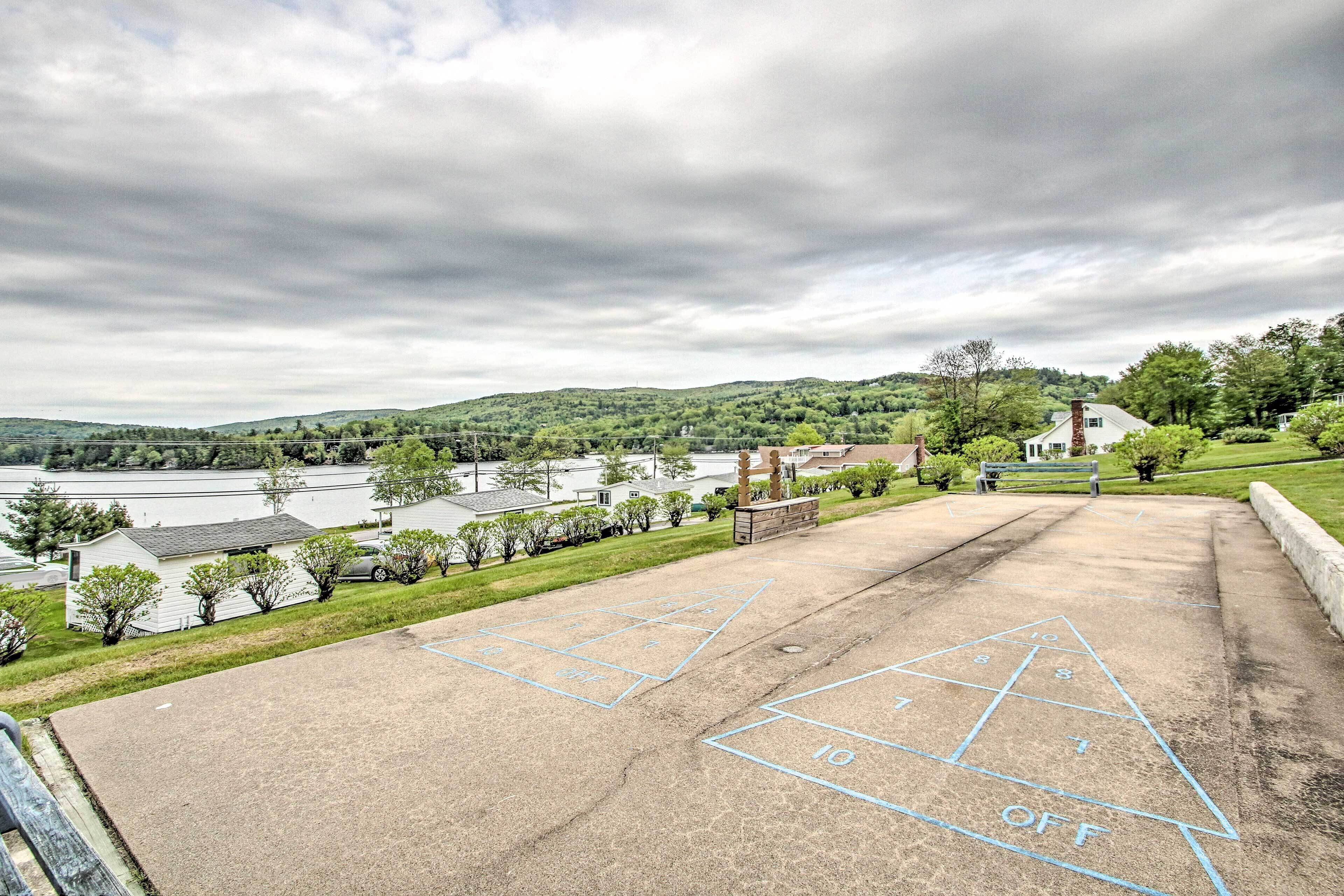 A park with a shuffleboard court, a bench, and a view of a lake and hills in the background.