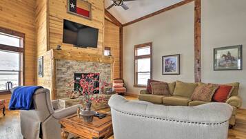 A spacious living room with a fireplace, wooden walls, a mounted TV, and a large window.