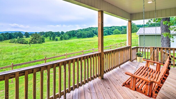 A wooden porch with a swing chair overlooking a green field.