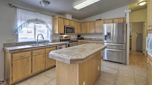 A kitchen with wooden cabinets, a central island, stainless steel appliances, and a window with a curtain. - 'red Rock Rambler' Moab Home w/ Hot Tub & Views! (Moab)
