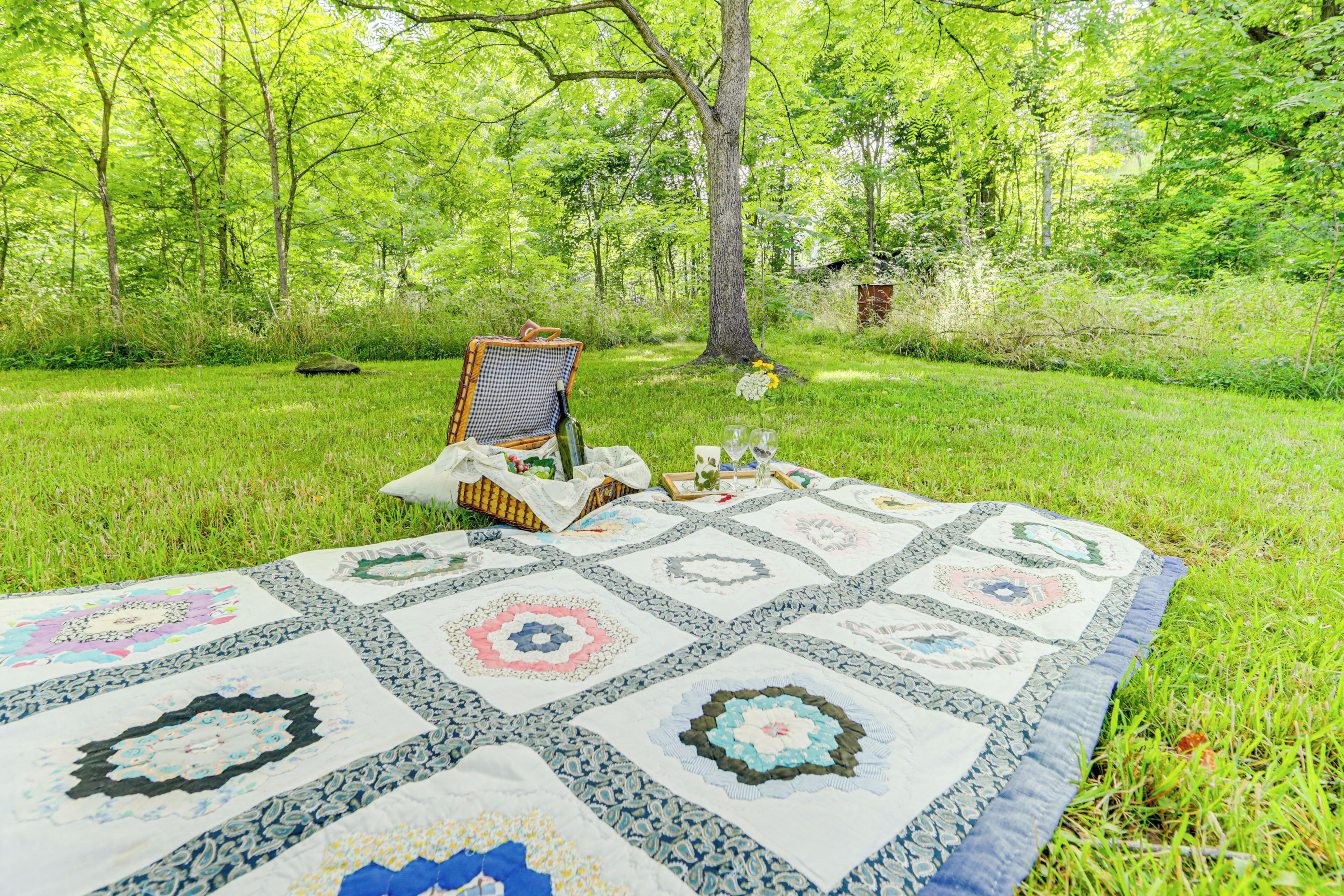 A quilt laid out on grass in a wooded area.