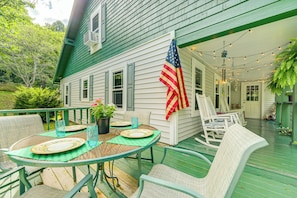 Une terrasse en bois peinte en vert, avec une table dressée pour quatre personnes, entourée de chaises en osier, et un drapeau américain accroché au mur.