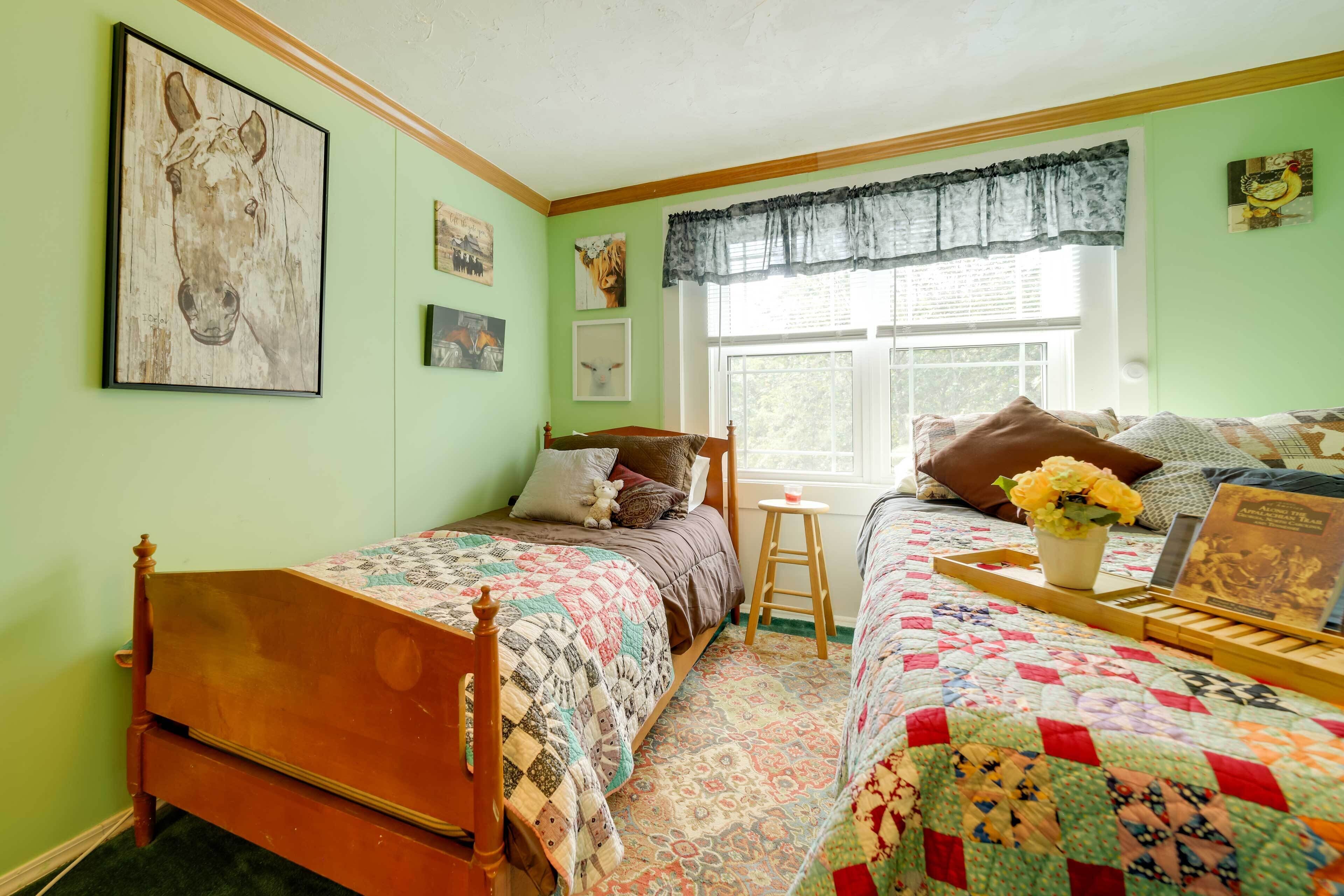 A room with two beds, a window with a lace curtain, and a wooden headboard.