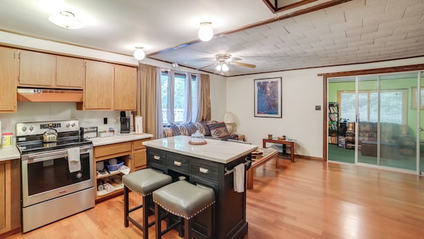 A spacious kitchen with wooden cabinets, a central island with stools, a built-in oven, and a ceiling fan. - Rustic Cottage With Fire Pit & Private Yard! (Fenwick)