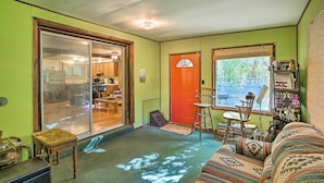 A cozy living room with a green wall, a sliding glass door leading to a kitchen, a red door, and a window with blinds. - Rustic Cottage With Fire Pit & Private Yard! (Fenwick)