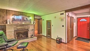 A room with a fireplace, a green leather sofa, a wooden bench, and a red door. - Rustic Cottage With Fire Pit & Private Yard! (Fenwick)