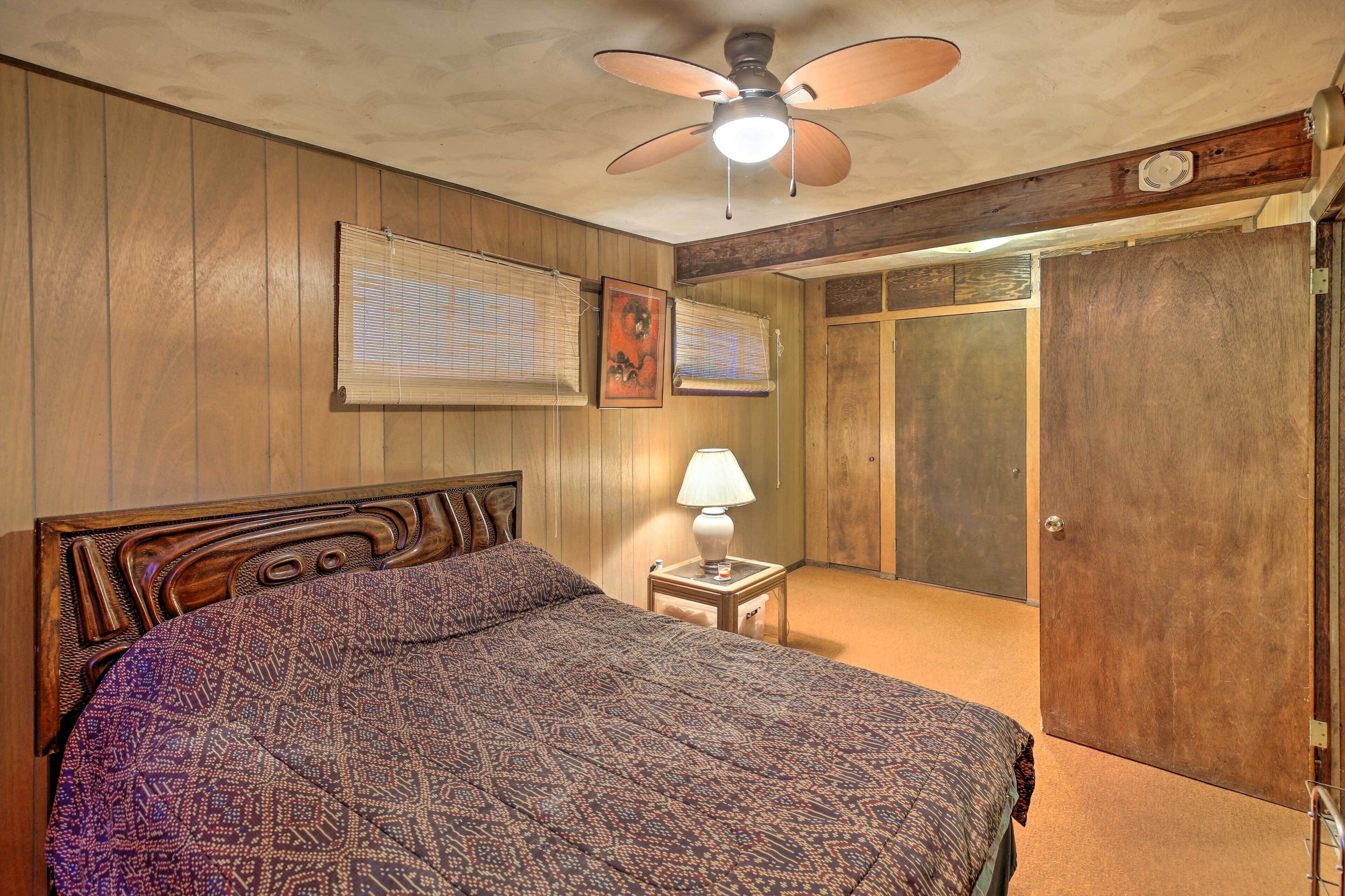 Une chambre à coucher avec une tête de lit en bois, une couvre-lit à motifs, une lampe de chevet et un ventilateur de plafond.