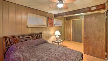 Un dormitorio con cabecera de madera, colcha estampada, lámpara de noche y ventilador de techo.