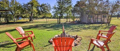 A grassy outdoor area with three red Adirondack chairs arranged around a central fire pit.