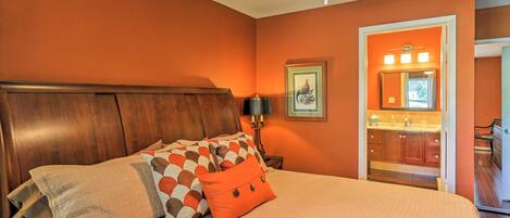 A bedroom with a wooden headboard, a bed with patterned pillows, a nightstand with a lamp, and a bathroom visible through an open door.