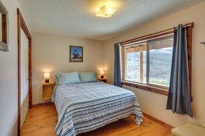 A bedroom with a bed, bedside lamps, a window with curtains, a framed picture on the wall, and a wooden floor.
