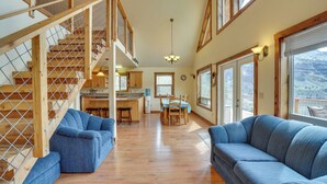 A spacious living area with a wooden staircase, a dining area, and large windows offering a view of the outdoors.