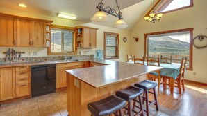 A kitchen with wooden cabinets, a dishwasher, a large island with bar stools, and a dining area with a view of mountains.