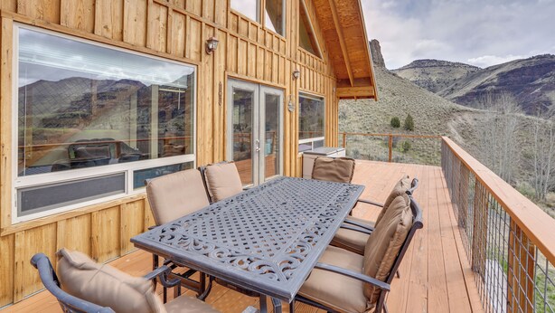 A wooden deck with a table and chairs, large windows, and a view of mountains.