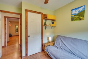 A room with a grey sofa, wooden floor, a white door, a shelf with books, and a painting on the wall.