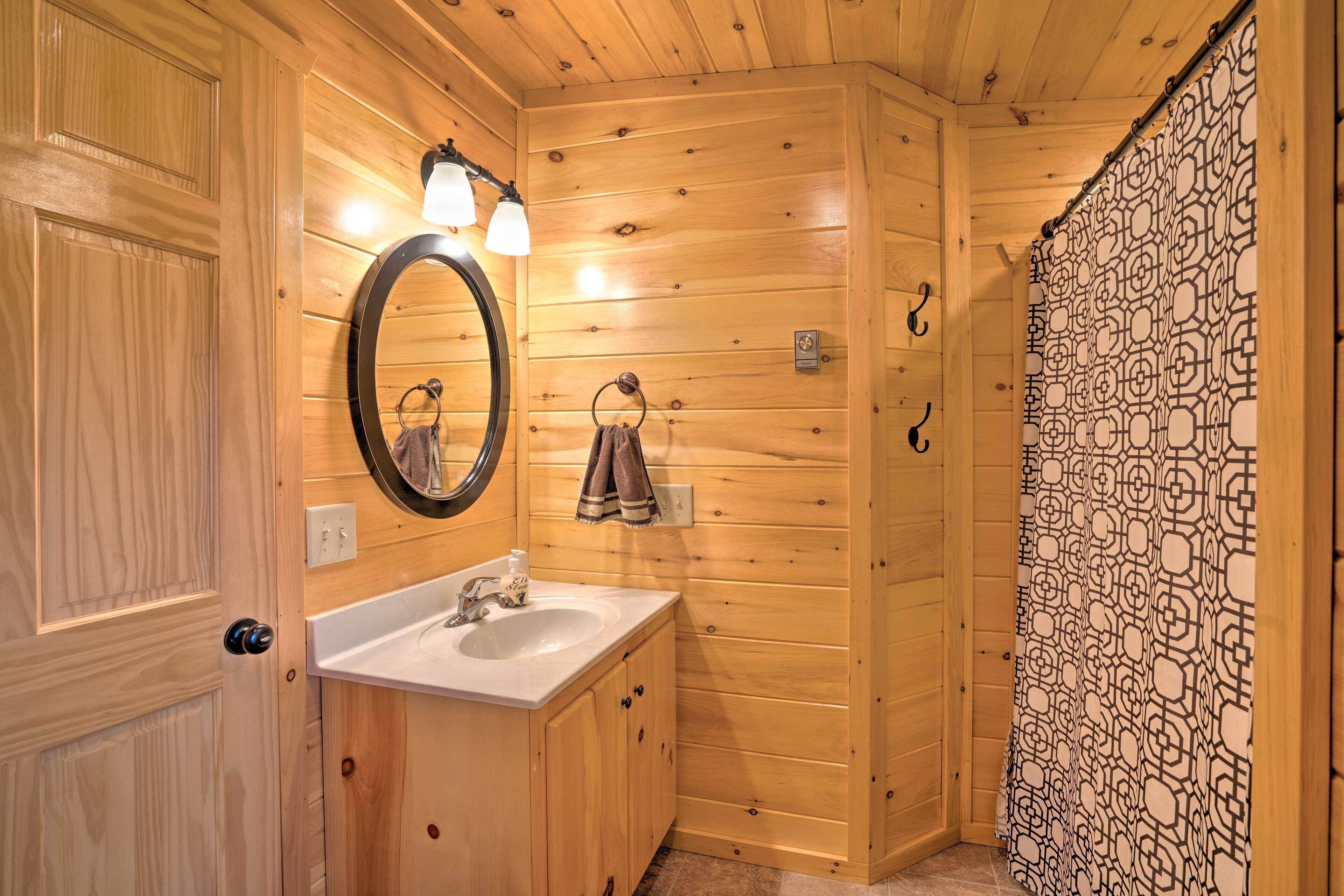 A wooden bathroom with a sink, mirror, towel ring, and patterned shower curtain.