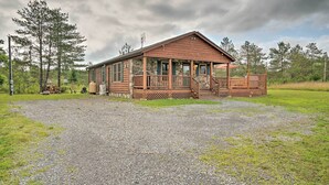 En træhytte med veranda, omgivet af grusvej og græsplæne, beliggende i et skovlandskab.